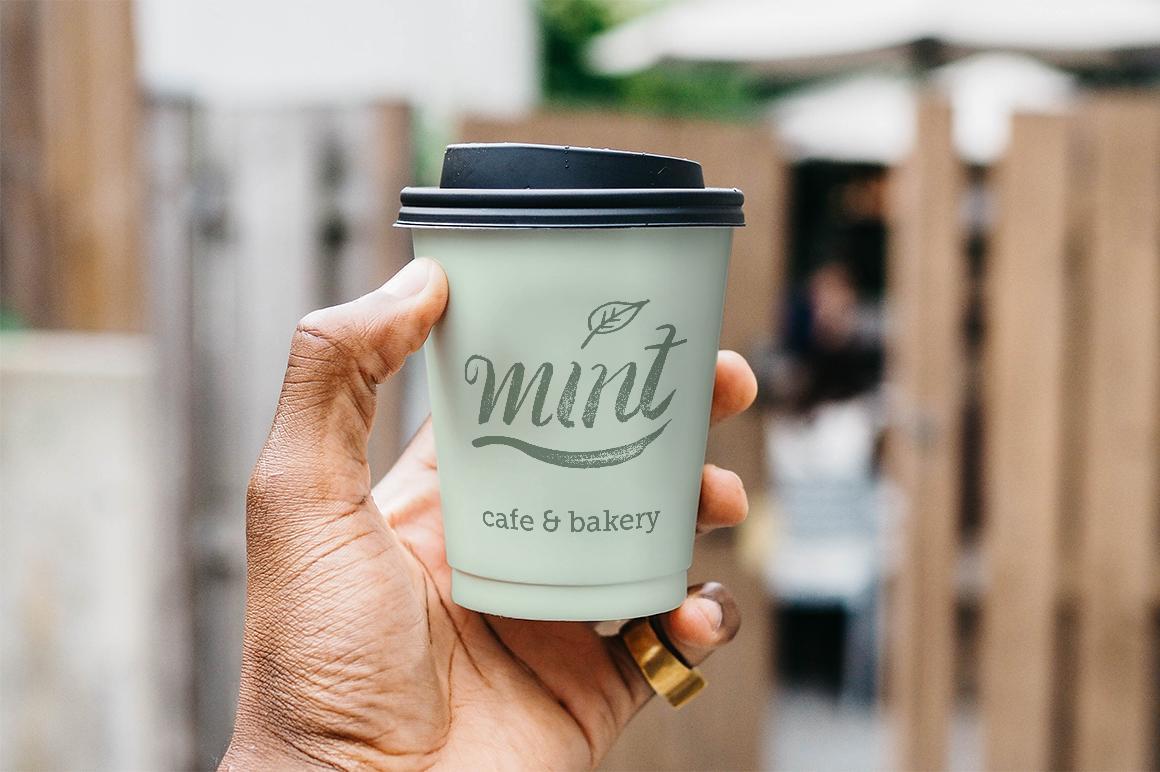 Hand holding a green coffee cup with Mint logo